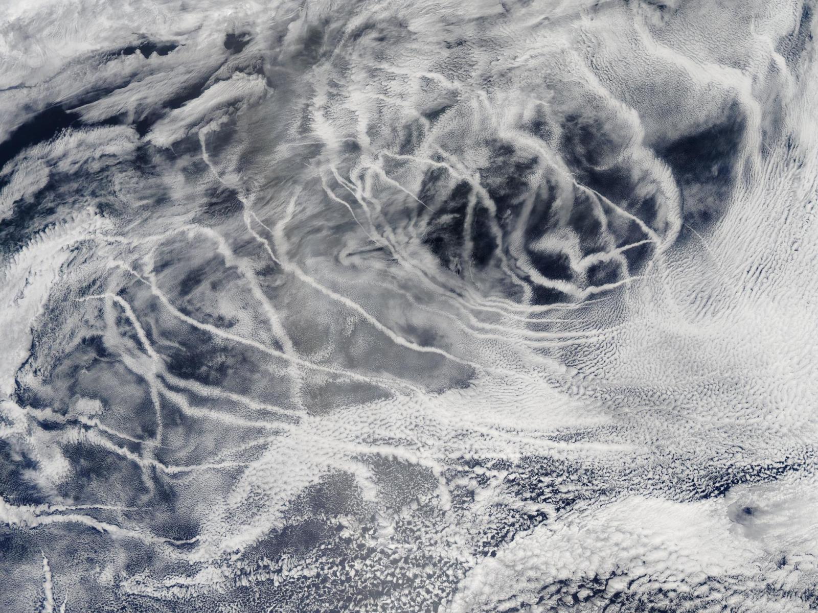 This aerial image depicts a portion of Earth's surface where typical white clouds are interspersed with thin, linear clouds that designate maritime shipping routes.