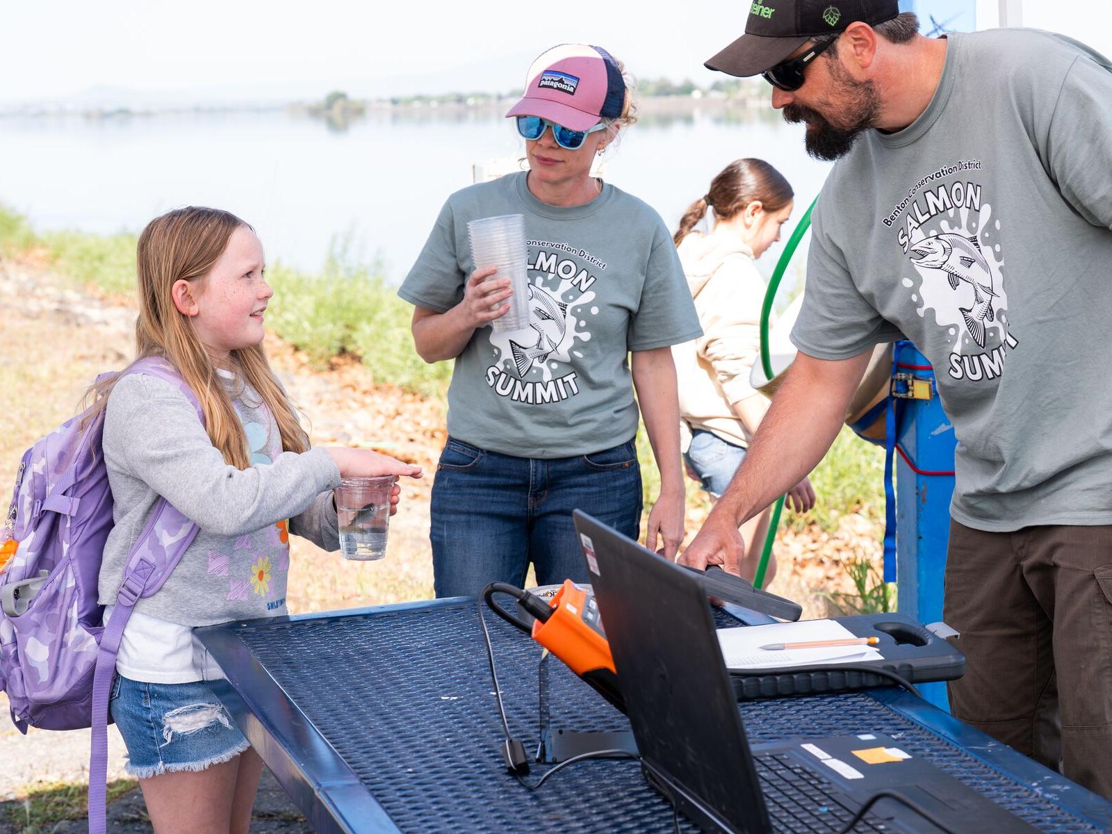 Student holds cup with salmon inside and talks to two STEM ambassadors
