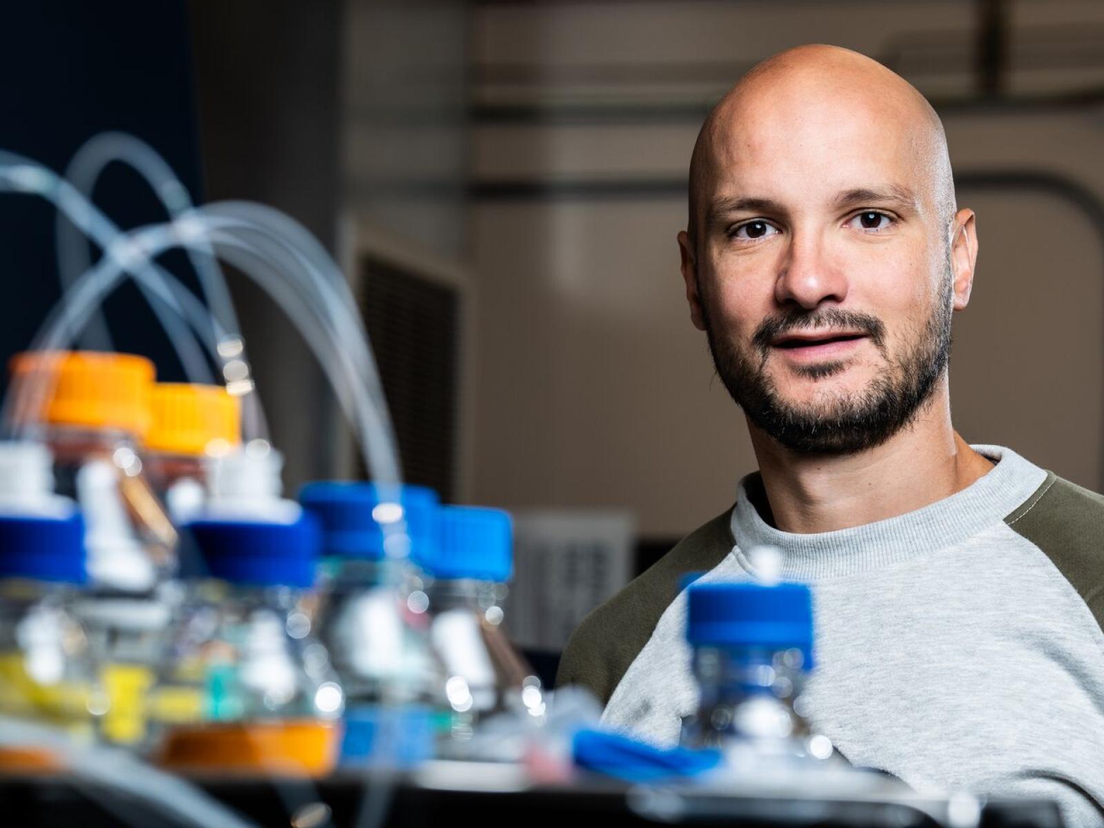 Dusan Velickovic smiles next to bottles with different colored caps and tubes