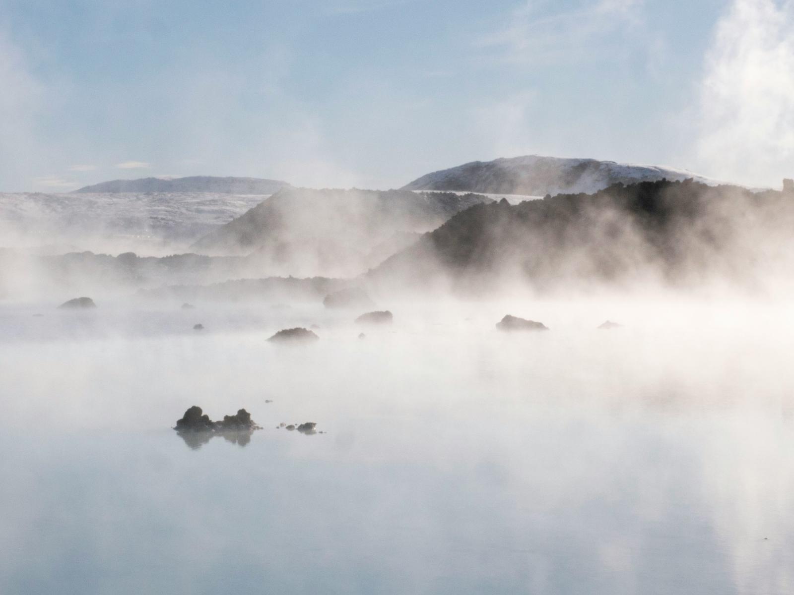 Steam rising off a lake, mountains in backdrop.