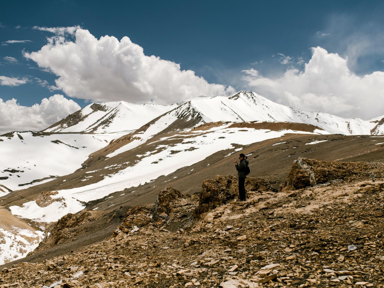 Photo of a person standing on top of mountain. There are scattered patches of snow behind them.