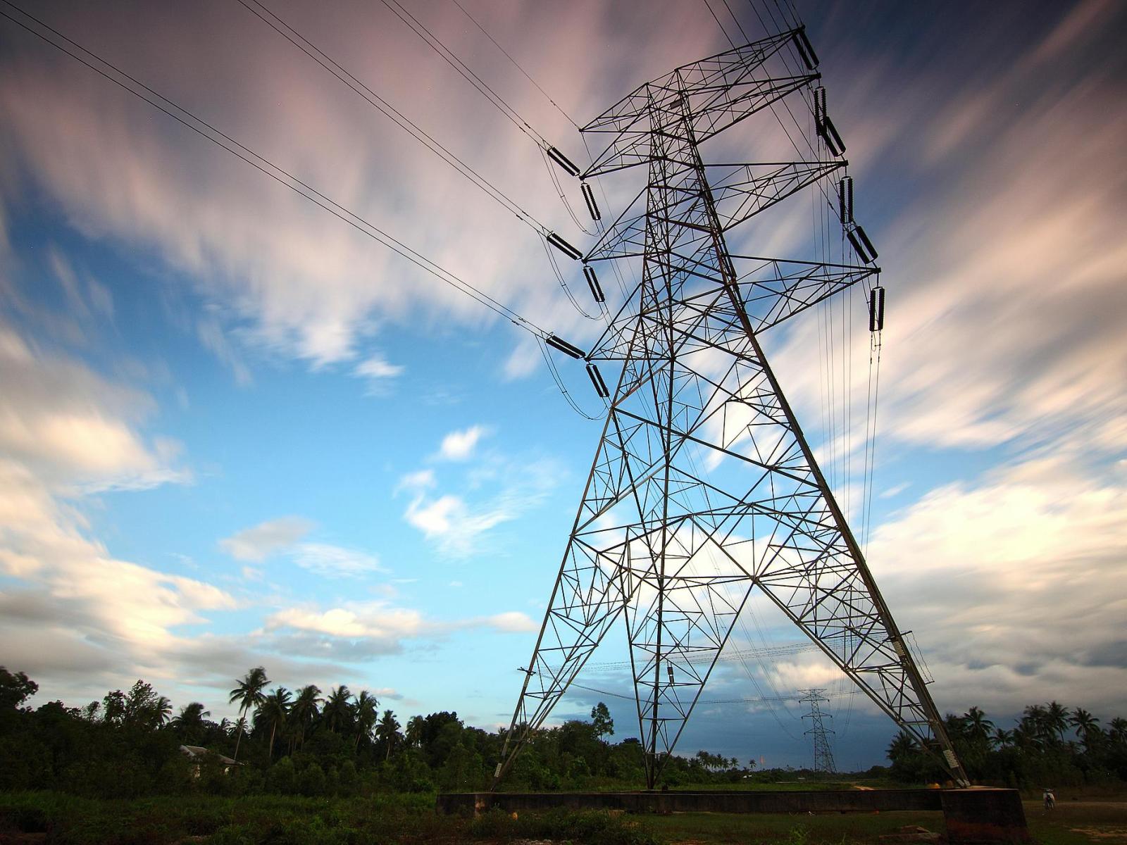 photograph shows a transmission tower against a cloudy, blue sky