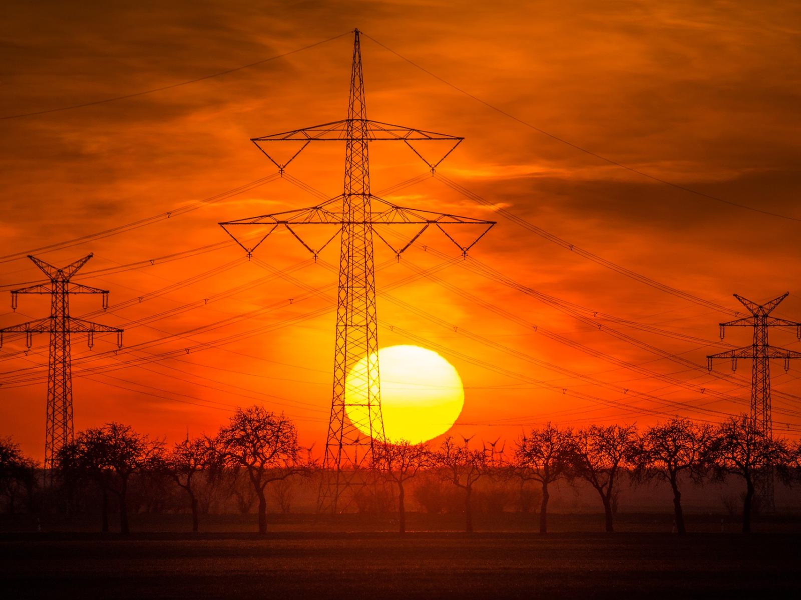 photograph shows powerline towers against a red and orange sunset