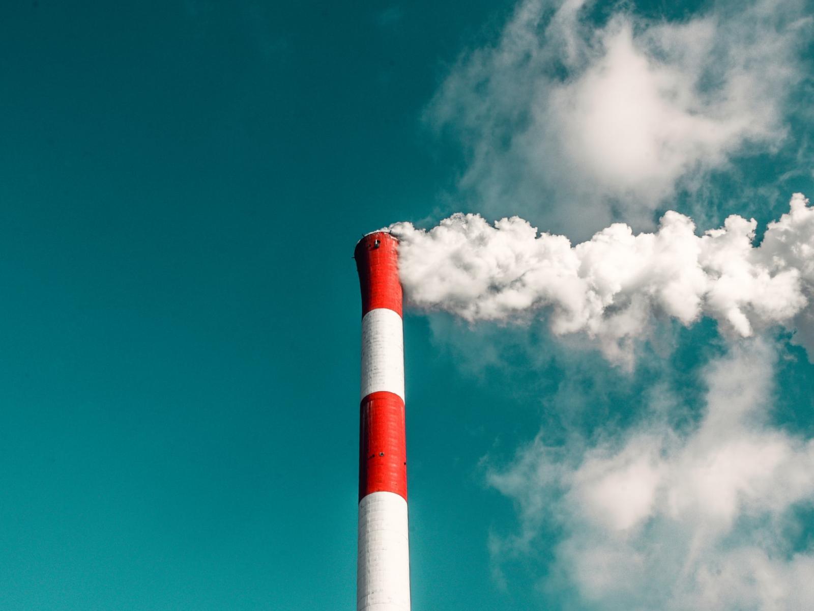 red and white striped smoke stack with white smoke against a blue sky