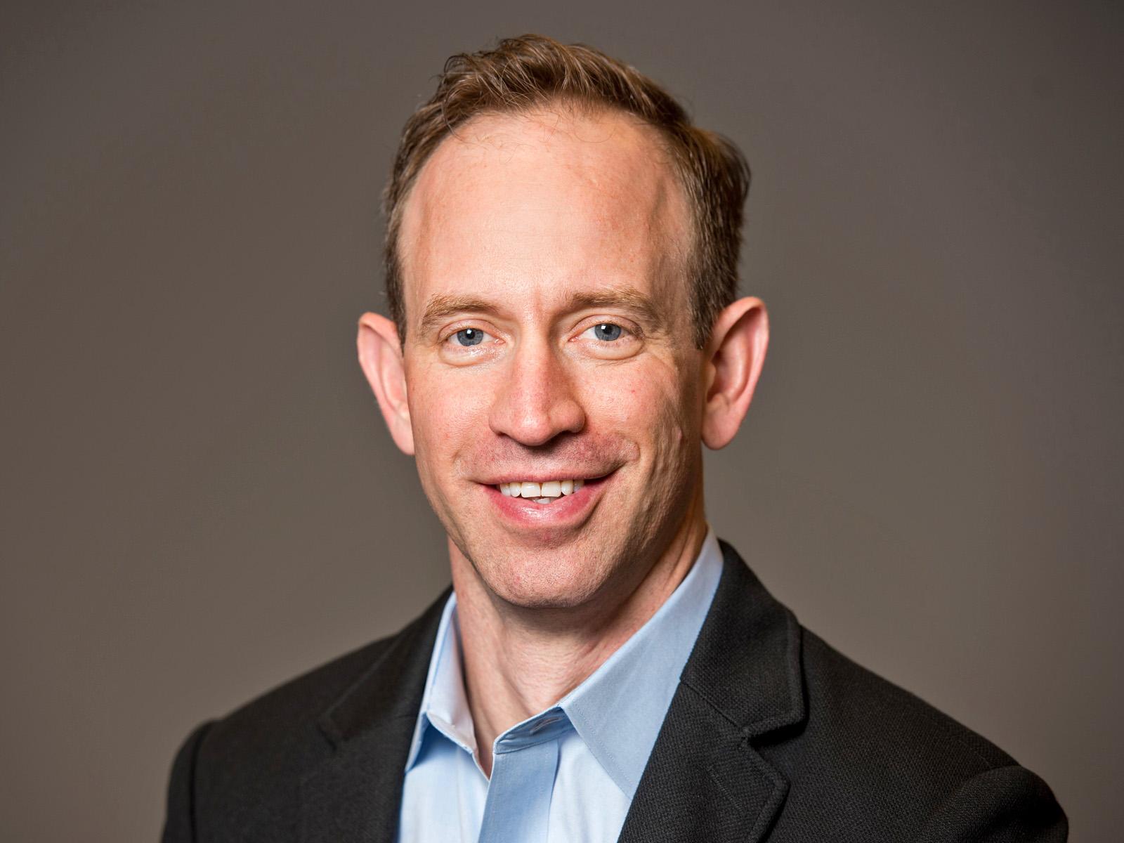 A researcher in a jacket and collared shirt smiles at the camera