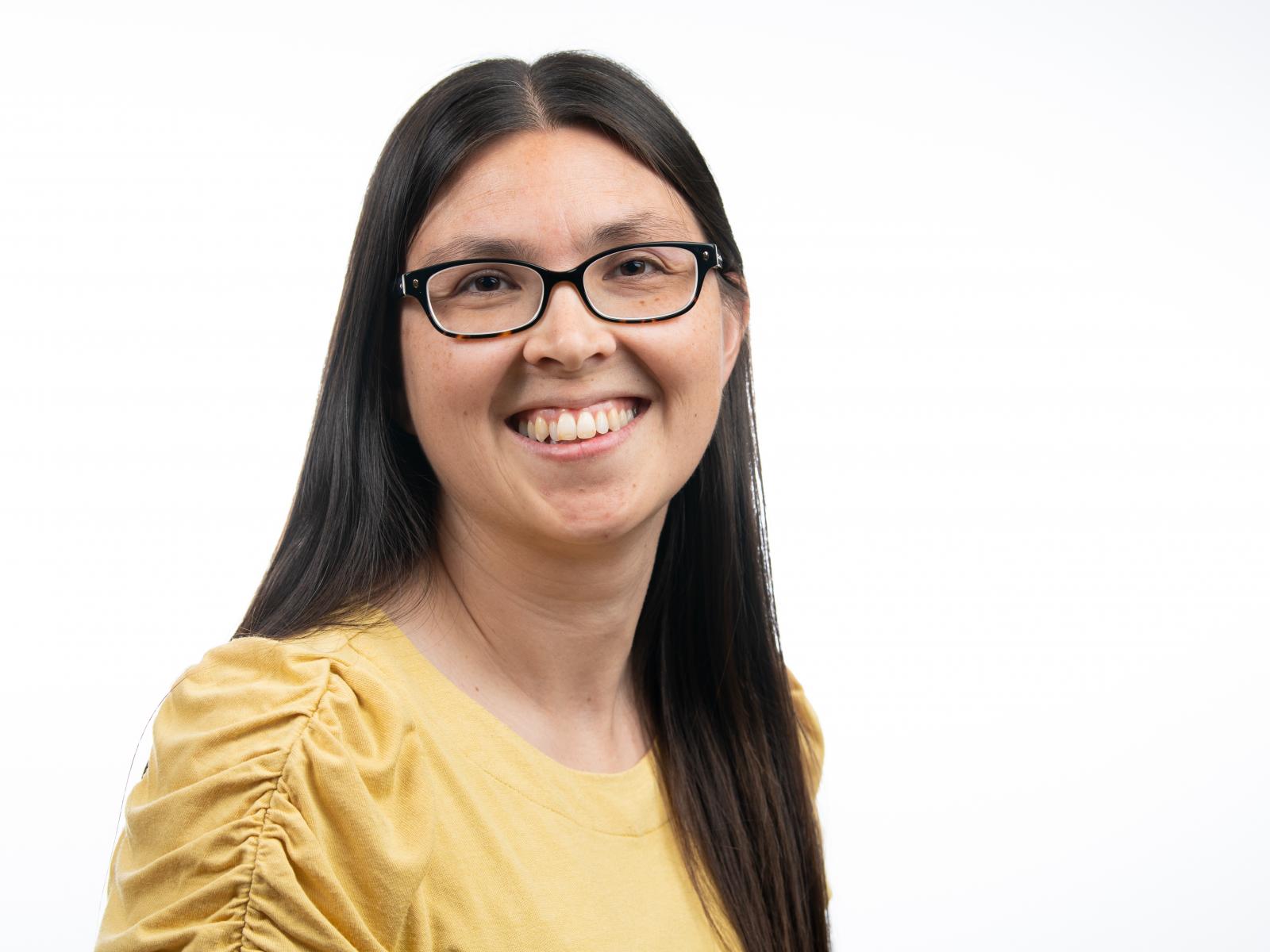 Photograph of a smiling woman wearing glasses and a yellow shirt