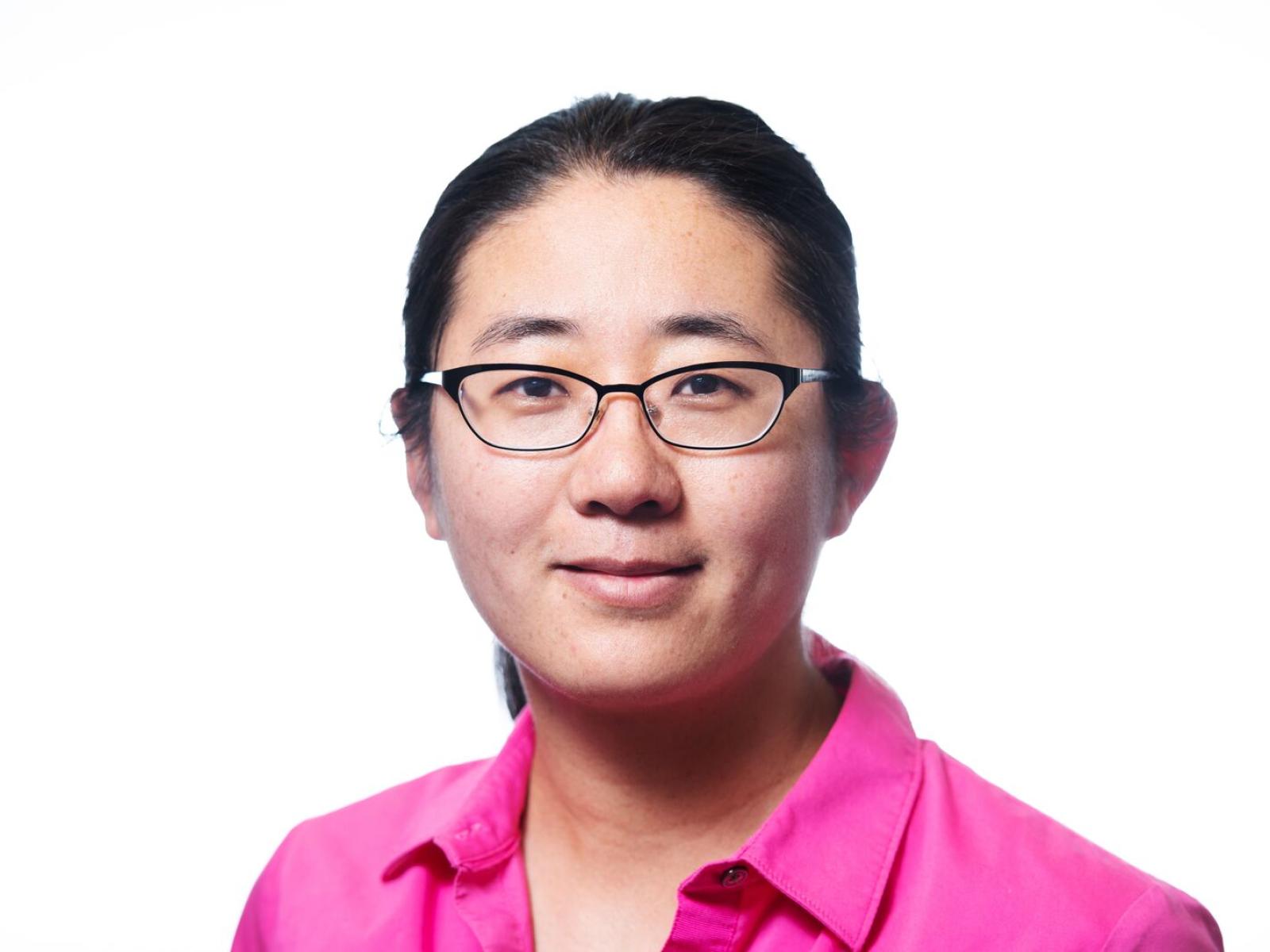 Headshot of a smiling woman with glasses, wearing a hot pink button down shirt