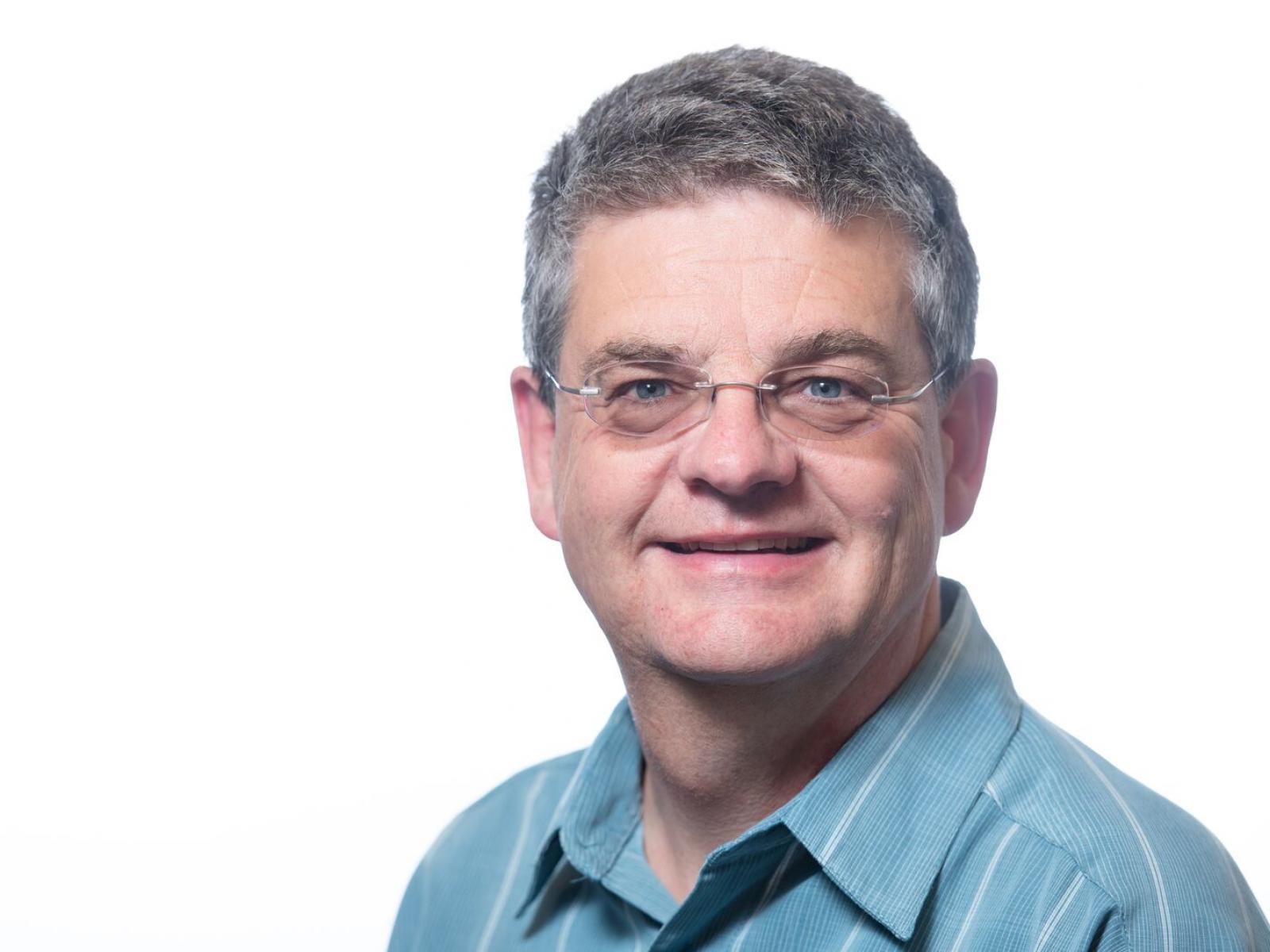 Photograph of a slightly smiling man wearing a blue collared shirt