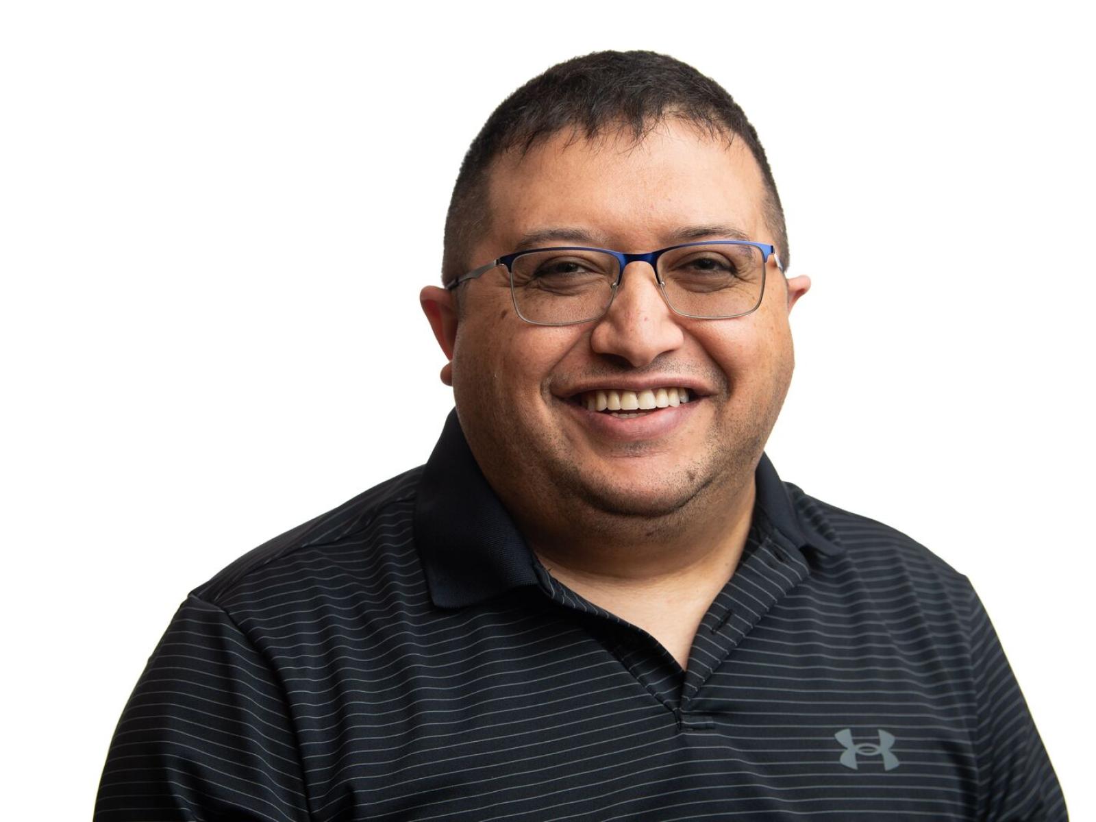 Omer Subasi, a man with short brown hair smiling. He wears glasses and a black collared shirt.