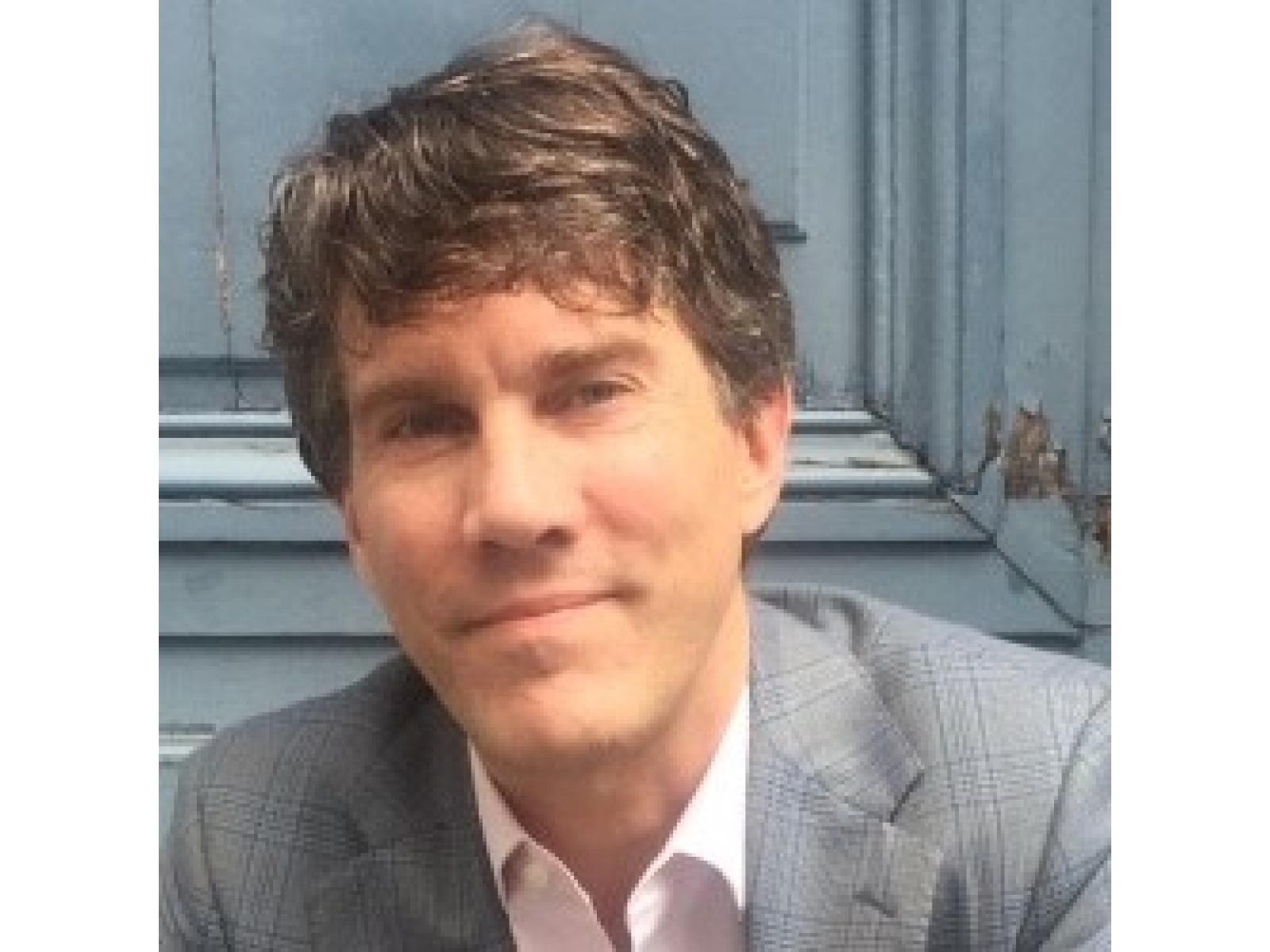 Photograph of a man wearing business attire against the background of a blue door
