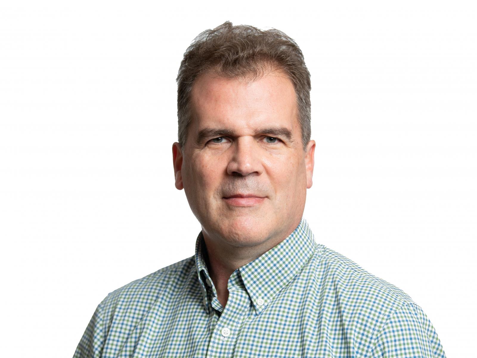 Photograph of a slightly smiling man wearing a patterned dress shirt