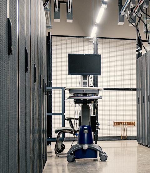 Image shows an aisle of black mesh cabinets holding data center servers.