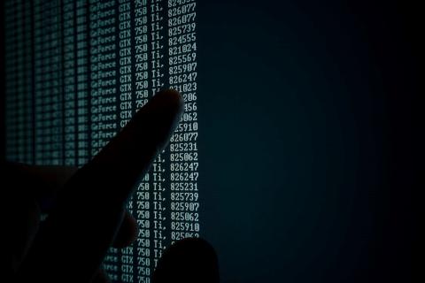 Finger touching a black computer screen with rows of green text