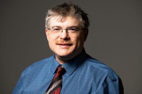 Person has glasses and is wearing a blue shirt with a necktie 