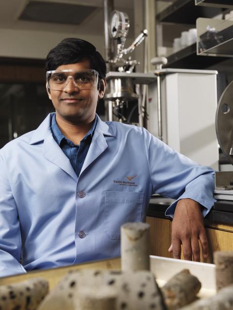 Researcher Praveen Thallapally wears a blue lab coat and is standing in a science lab
