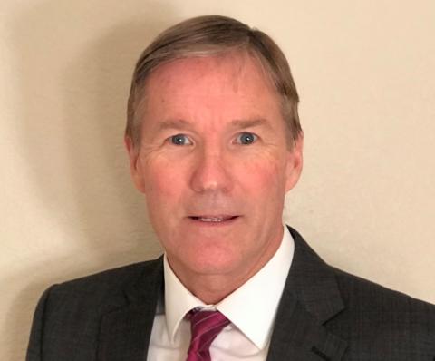 Mark Byrnes is a middle-aged white man wearing a red tie and a black suit jacket.