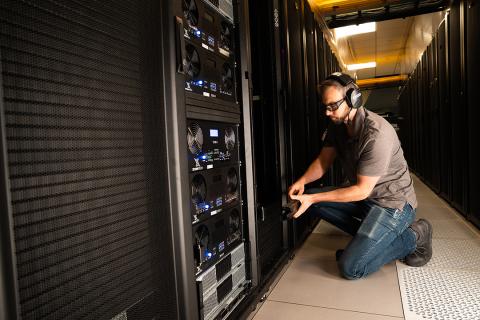 a technician in safety goggles and ear protection works on a server rack