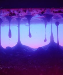 a pink, blue and purple close-up view of thick "sludge" moving through space in droplets