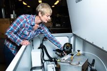 Carolyn Pearce reaches her left arm into a large white box that protects X-ray absorption spectroscopy instrumentation, used to determine the chemical state and local bonding structure for an atomic species in materials such as catalysts, sensors, biomaterials, thin films, and batteries.