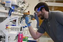 Photograph of a man, holding a glass jar in a laboratory