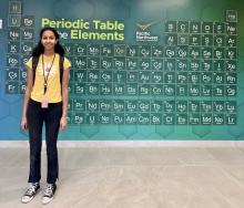 Hosanna Tesfa, a senior at Hanford High School, is a summer 2024 intern at PNNL. She is standing in front of a large periodic table on the wall in the Energy Sciences Center.
