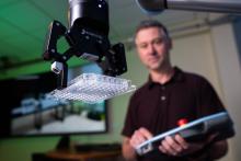 A researcher with a control device standing behind a robotic arm holding a lab sample tray.