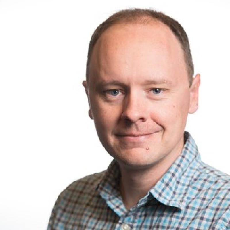 Photograph of a slightly smiling man wearing a collared shirt