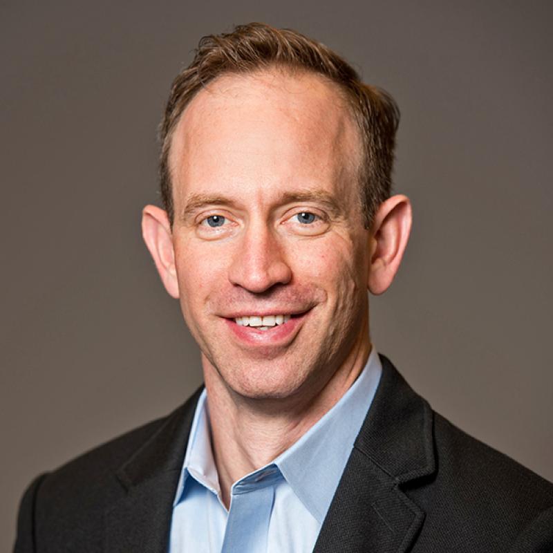 a researcher in a jacket and collared shirt smiles at the camera