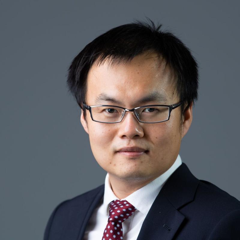 Man wearing glasses with dark sports jacket, white shirt, and multi-colored tie.