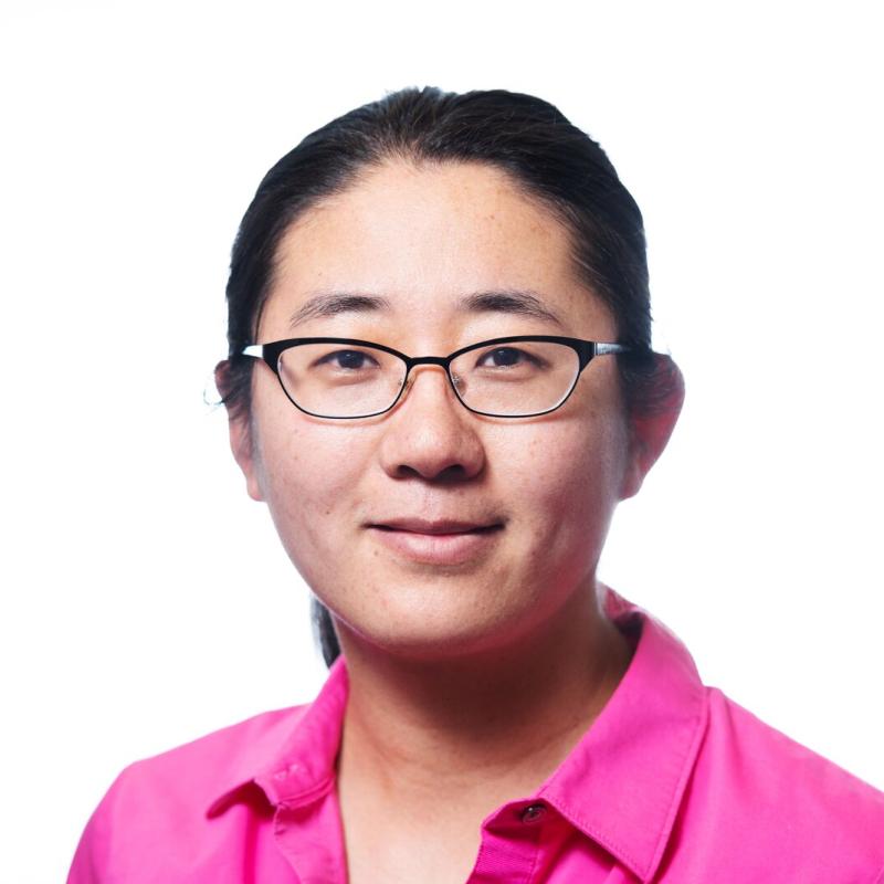 Headshot of a smiling woman with glasses, wearing a hot pink button down shirt
