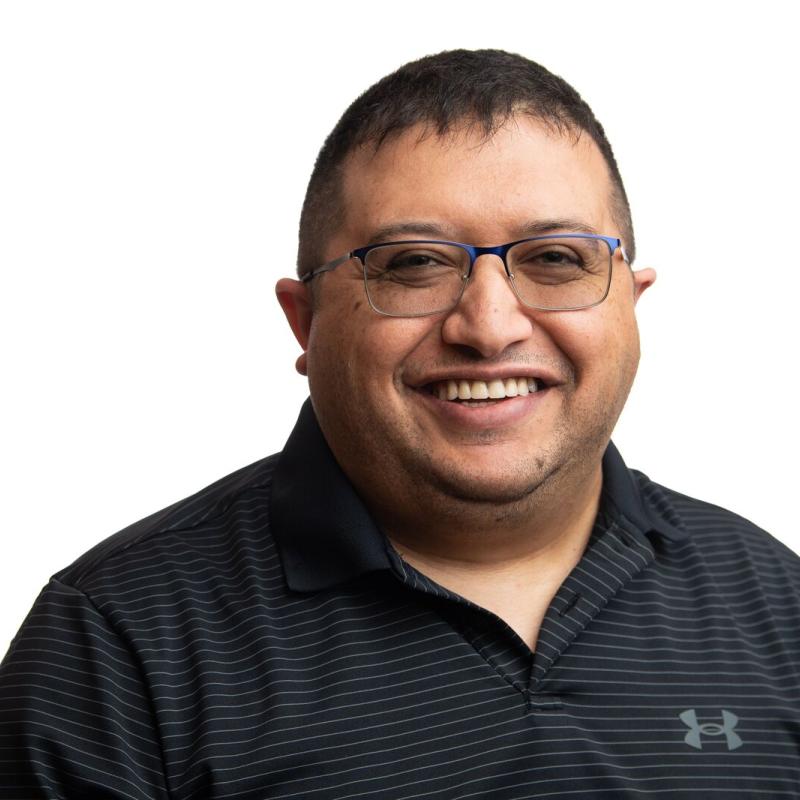 Omer Subasi, a man with short brown hair smiling. He wears glasses and a black collared shirt.