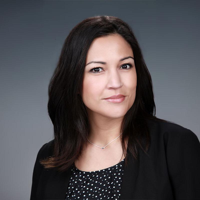 headshot of Nicole Castilleja-Bentley, pictured looking toward the camera in a black blazer against a great background