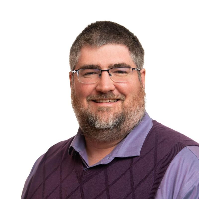 Headshot of Stephen Young, wearing glasses, a light purple collared shirt and dark purple vest