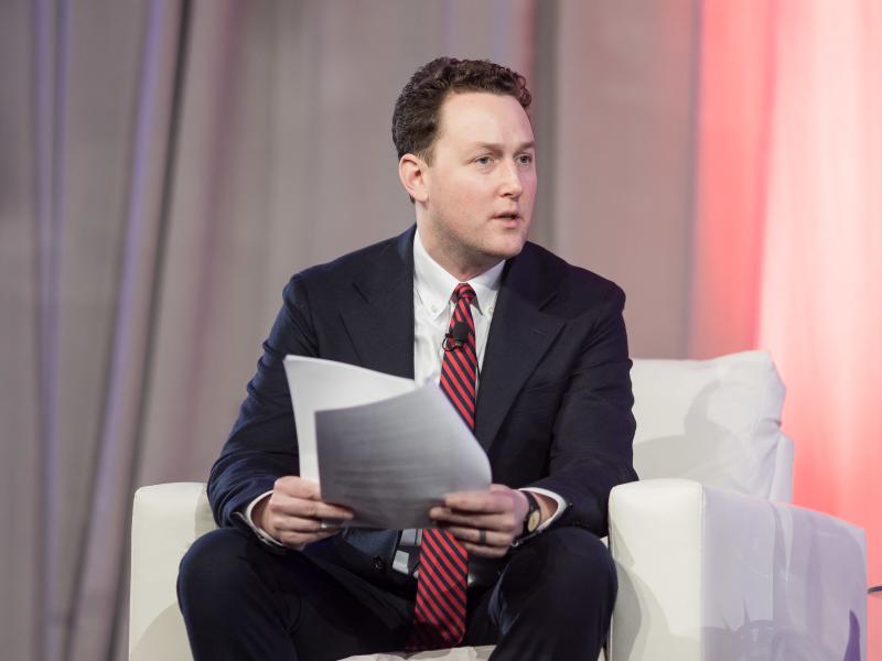 John VerWey sitting in a chair moderating a panel with papers in his hand. 
