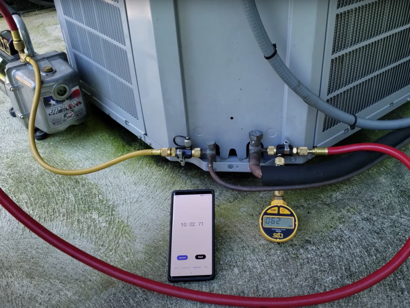 A smartphone device next to an air conditioning unit with two hoses attached 