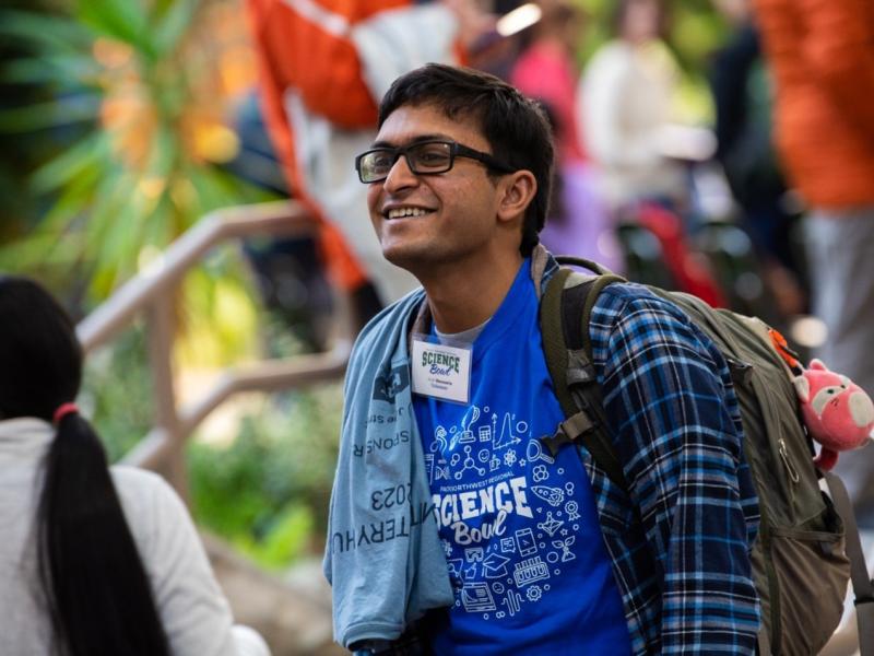 Arpit Ranasaria, smiling. Wearing glasses, blue shirt, flannel shirt, and a backpack.