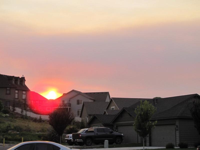 Sunset over rooftops with a hazy sky due to wildfire smoke
