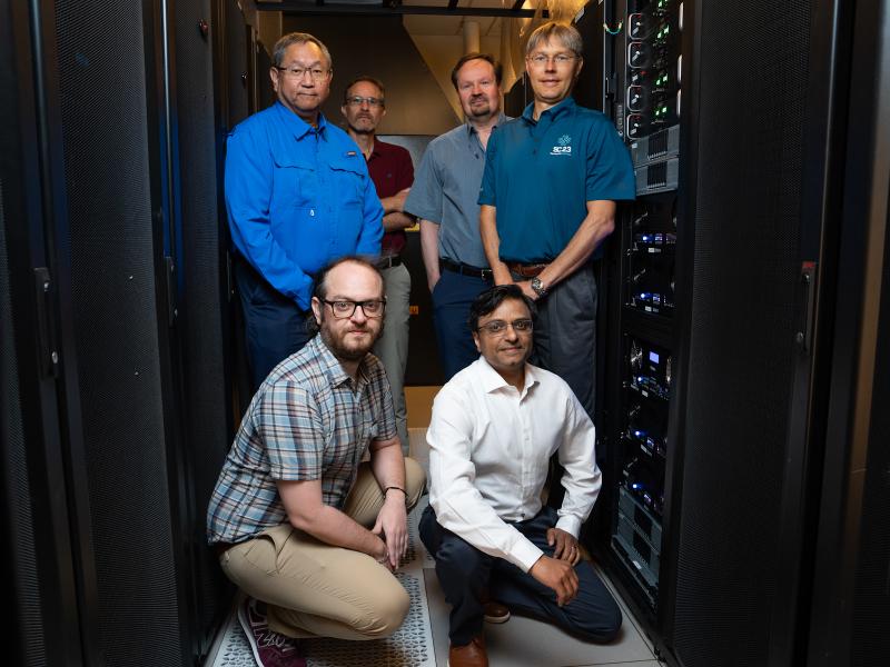 Group photo of six men with a computer