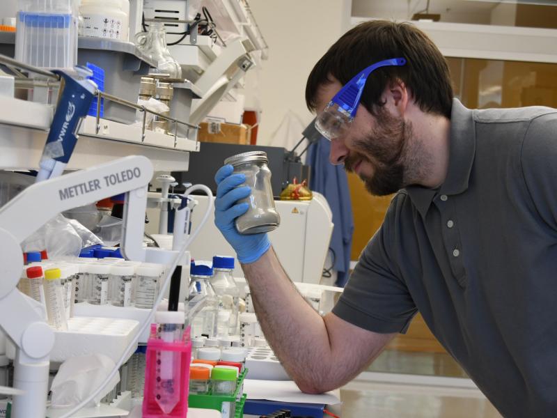 Photograph of a man, holding a glass jar in a laboratory
