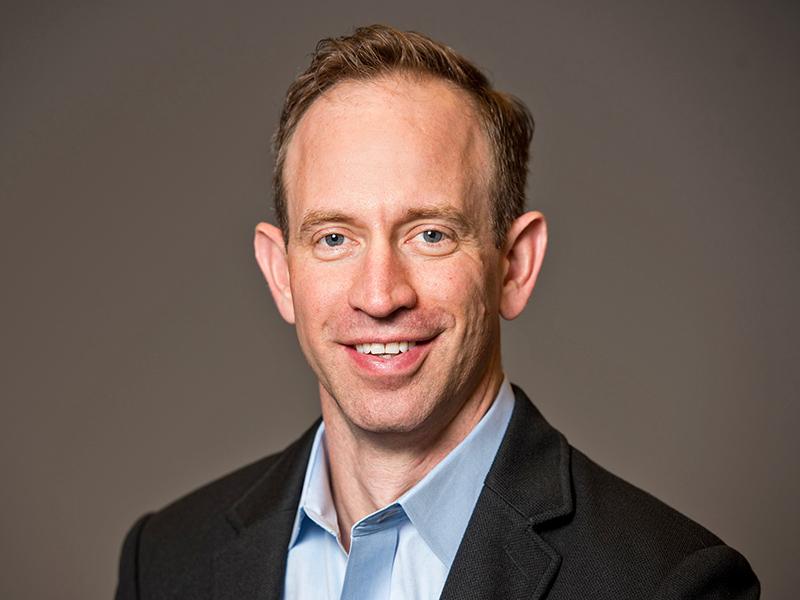 a researcher in a jacket and collared shirt smiles at the camera
