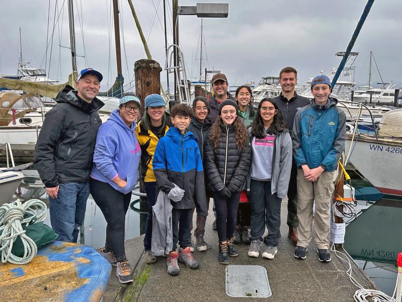 team members and coaches of the Intelligent Mavericks team and researchers at PNNL standing on the dock at John Wayne marina on a cloudy day