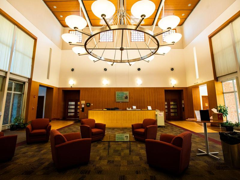 a warmly lit building lobby with a large round hanging light fixture, armchairs, a reception desk and a sign on the wall that reads "Environmental Molecular Sciences Laboratory"