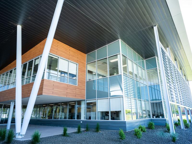 a multilayer, angular building facade with large white pillars supporting the roof and a concrete walkway and entry plaza