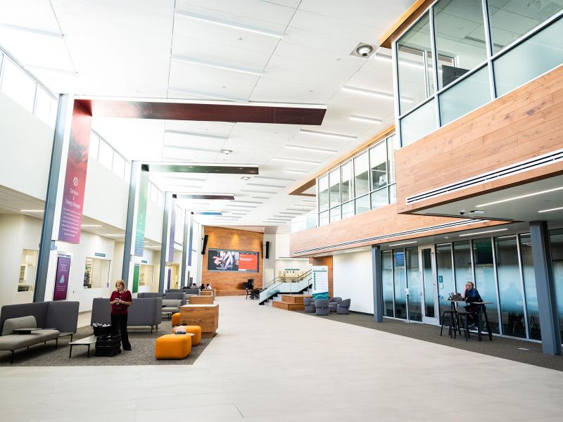 a light and airy interior building lobby with high ceilings and tall glass windows, couches, tables, and chairs