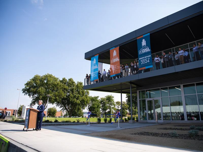 Lab director Steven Ashby speaks at a podium in front of the newly-dedicated GSL while smiling researchers observe from a second-floor patio