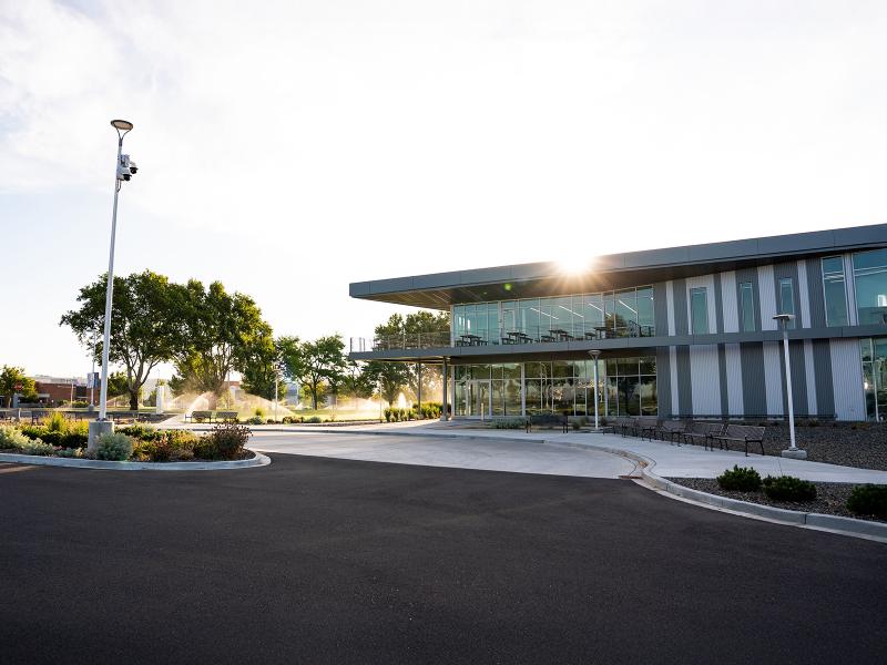 a two-story glass and brick building with an asphalt driveway and irrigation fountains on a grass lawn