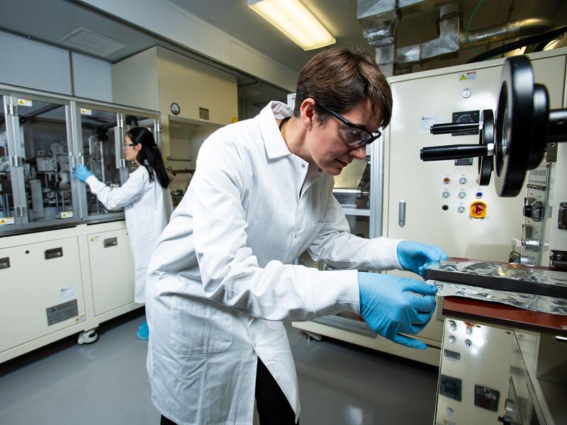Researchers in white lab coats, protective eyewear and blue safety gloves working with equipment in a sterile lab