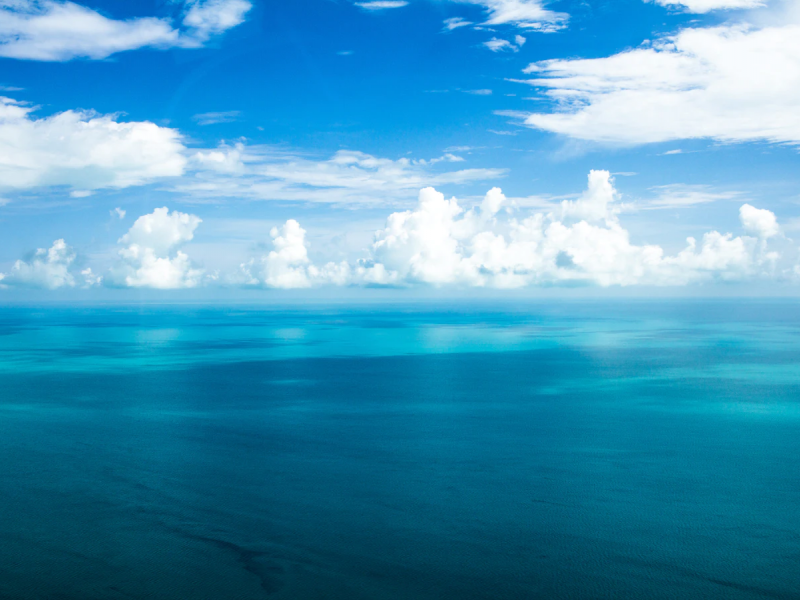 White clouds in a blue sky above bright blue water