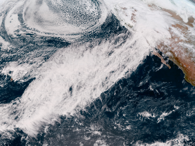 Satellite image of a line of clouds, known as an atmospheric river, over the Pacific Ocean moving onto the southern coast of California and northern Mexico