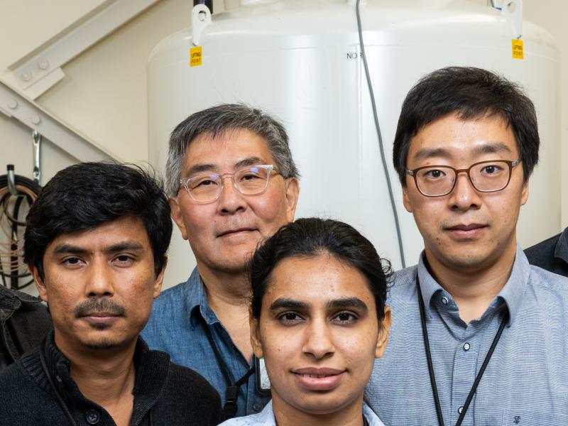 Photograph close up of the faces of four researchers standing in front of an NMR